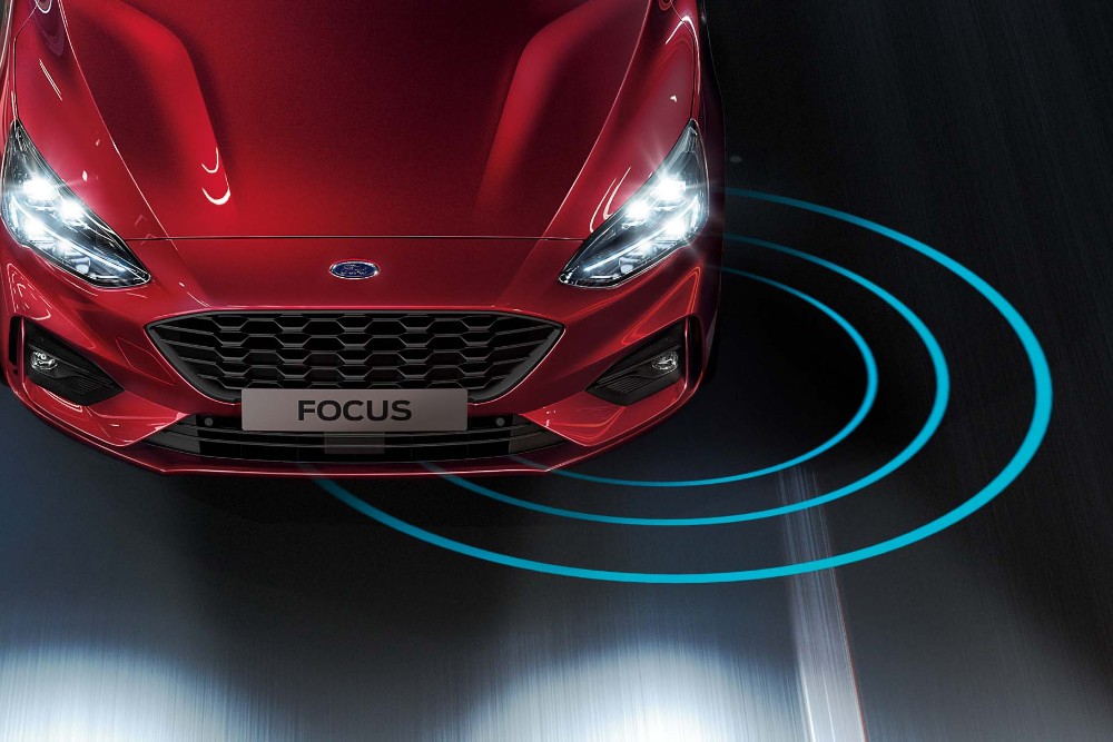 A red Ford Focus on the road, with radiating blue lines indicating a driver-assist feature.