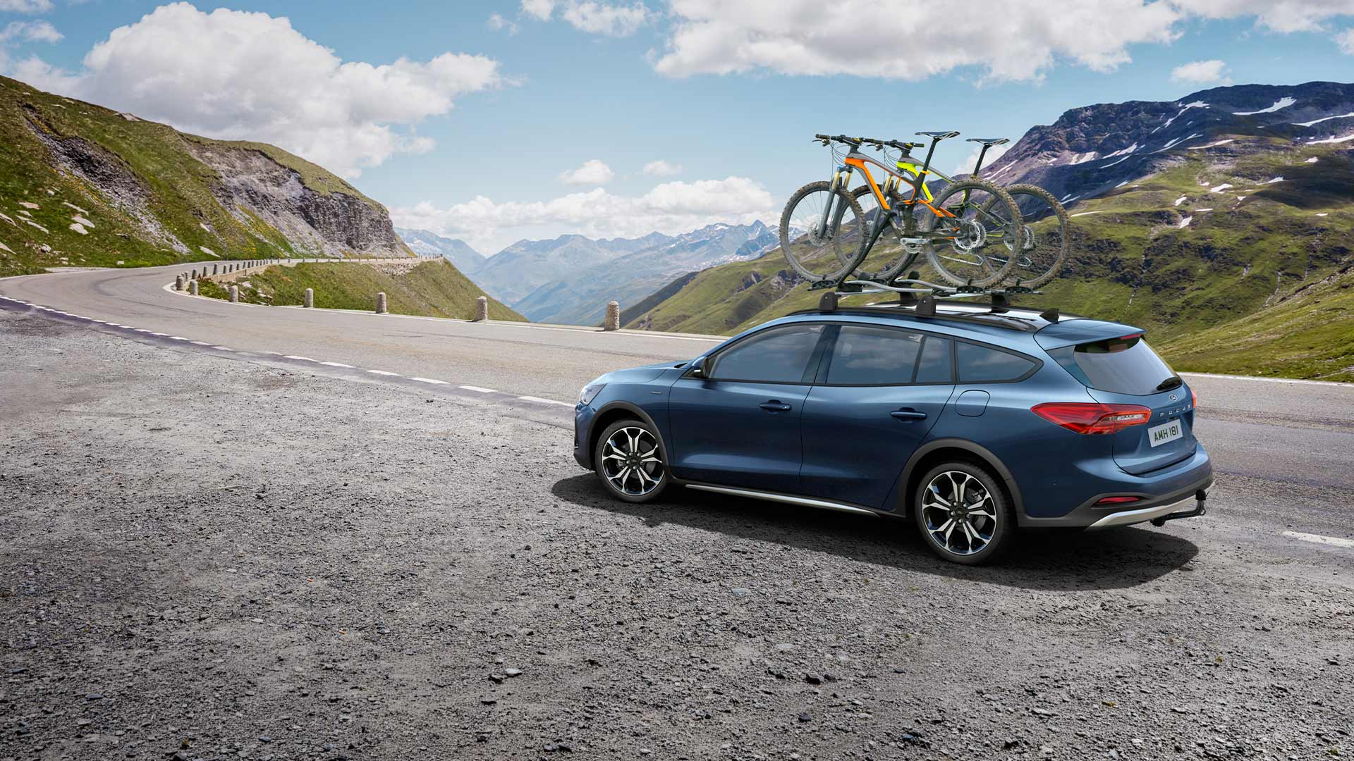 A blue Ford Focus estate with bicycles on the roof rack, parked on a mountain road.