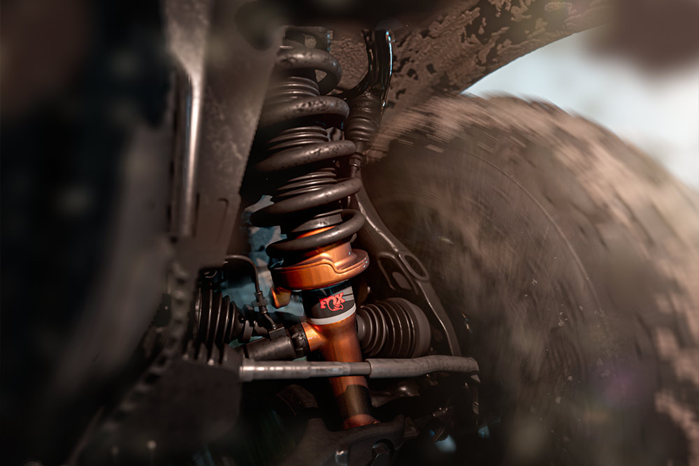 Close-up of a vehicle's suspension system, featuring an orange shock absorber and coil spring.
