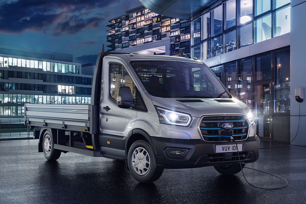 Silver Ford Transit chassis cab parked in front of a modern building at night.