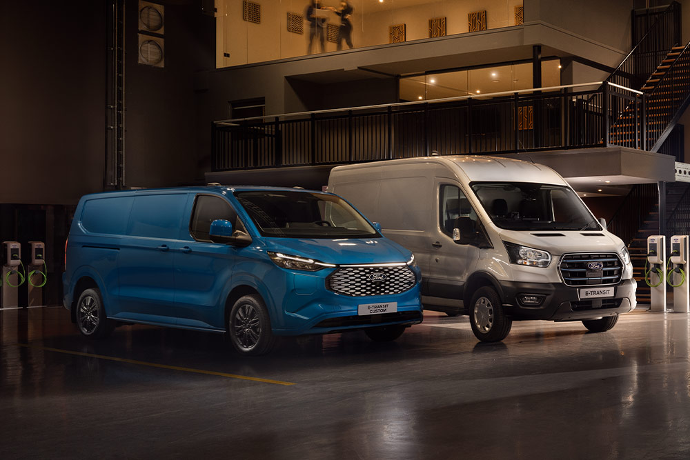 A blue Ford E-Transit Custom and a silver Ford E-Transit charging in a car park.