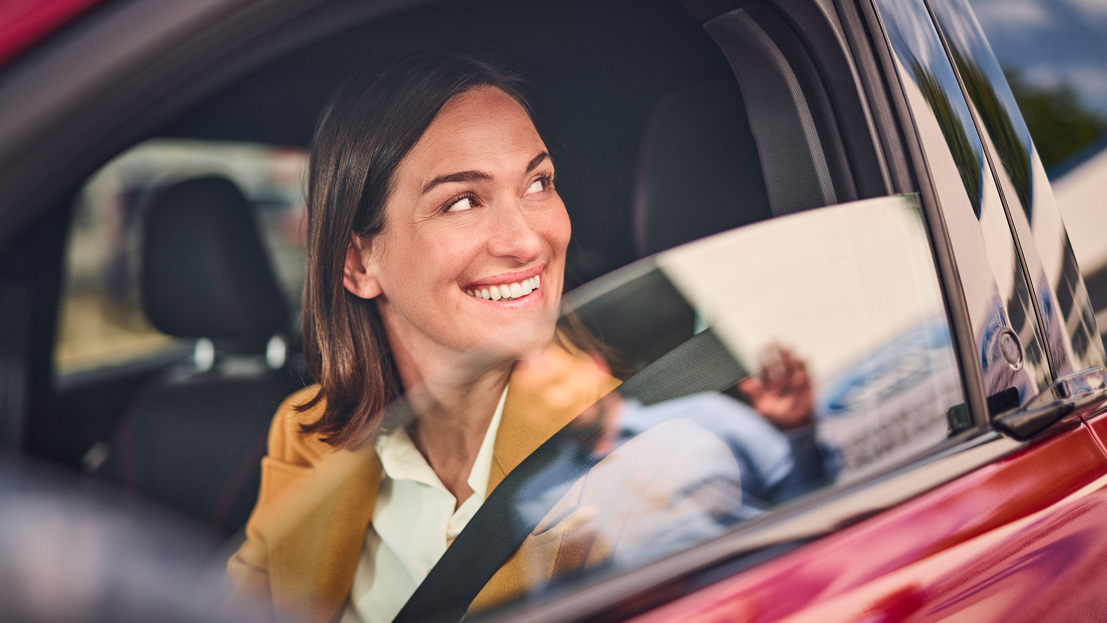 A person smiles while sitting in a red Ford car. 