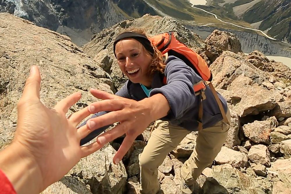 Hiker reaching for helping hand on rocky mountain ridge.