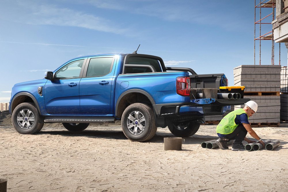 Blue Ford Ranger pickup truck at a construction site, with a worker handling pipes near building materials.