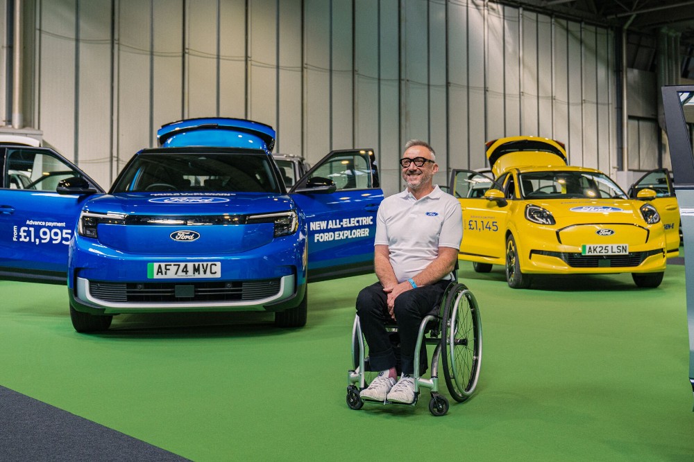Jason Richards in a wheelchair with a blue Ford Explorer and a yellow Ford Puma Gen-E at an event.