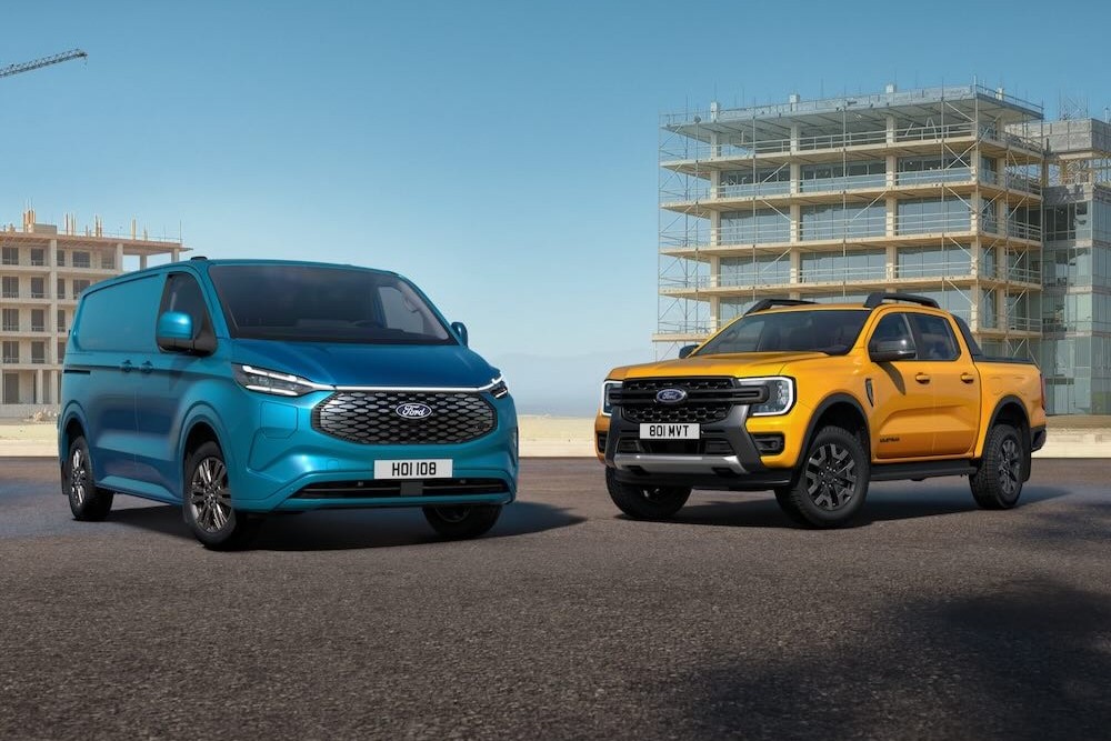 A blue Ford Transit Custom van and an orange Ford Ranger parked in front of buildings under construction.